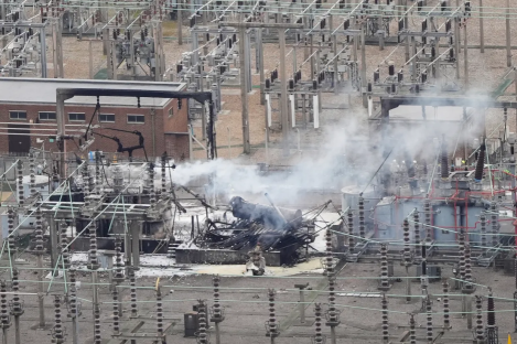 Aerial view of a damaged electrical substation with smoke and fire.