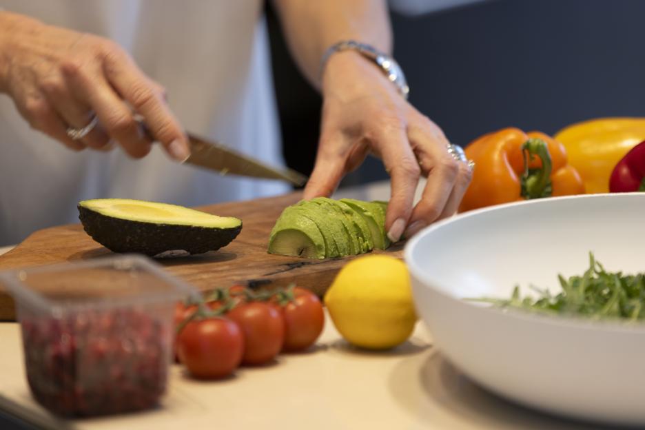 Woman slicing avocado on a wooden board.