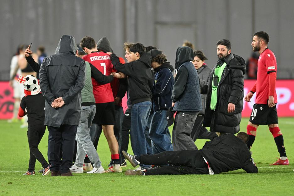 Fans rush the field as a Georgian soccer player leaves the pitch.