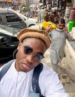 Selfie of a man in a white thobe and sunglasses in a busy street.
