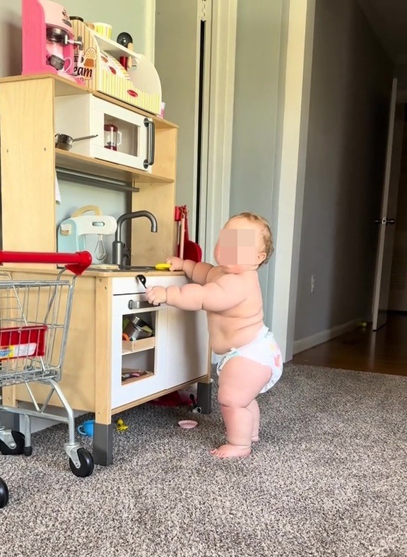 A chubby baby playing with a toy kitchen.