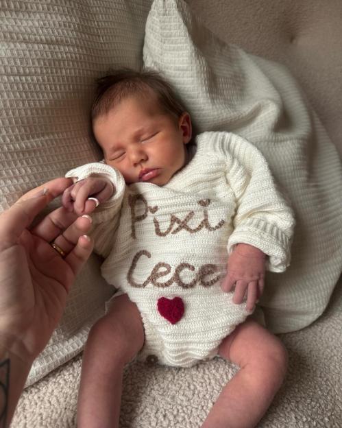 Baby Pixi CeCe sleeping on a blanket, holding an adult's finger.