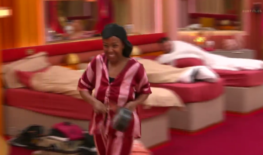 Screenshot of a woman in striped pajamas smiling while walking past beds in a bedroom.