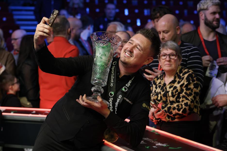 Kyren Wilson of England holding the Players Championship trophy and taking a selfie with a fan.