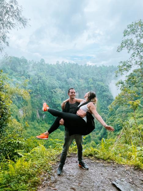 A man carrying a woman in his arms, overlooking a lush green landscape.