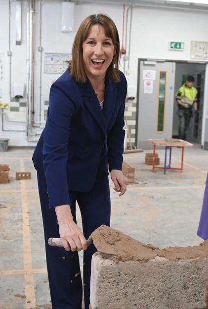 Rachel Reeves, Chancellor of the Exchequer, using a trowel to apply mortar to a brick.