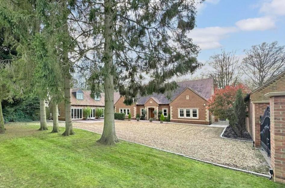 A large brick house with a gravel driveway, surrounded by trees and a lawn.