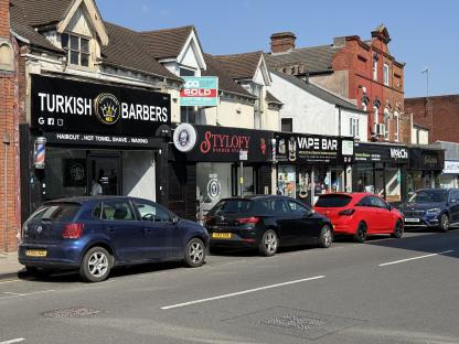 Harborne, Birmingham street scene with shops and parked cars.
