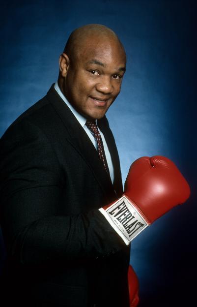 Portrait of George Foreman in a suit holding a boxing glove.