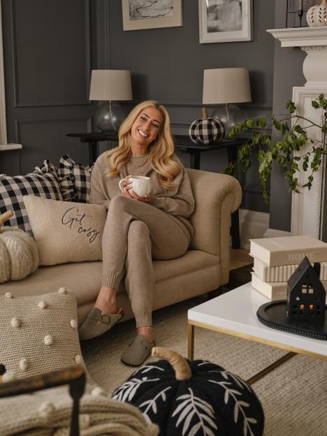 Woman relaxing on a couch in a cozy living room, holding a mug.