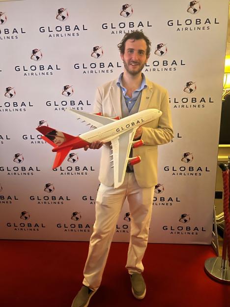 Man in beige suit holding a Global Airlines model airplane.