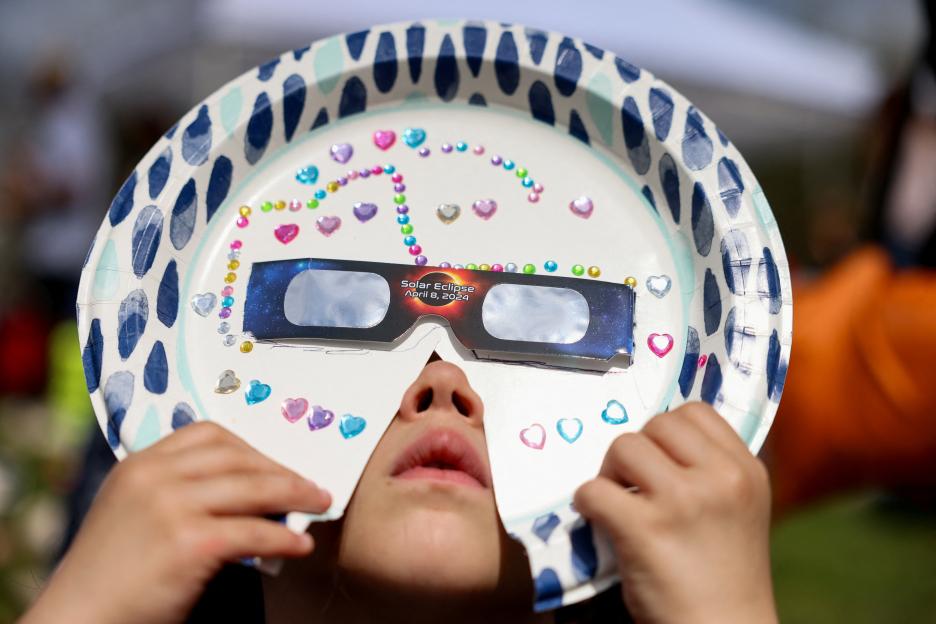 Child viewing a partial solar eclipse through a decorated paper plate viewer.