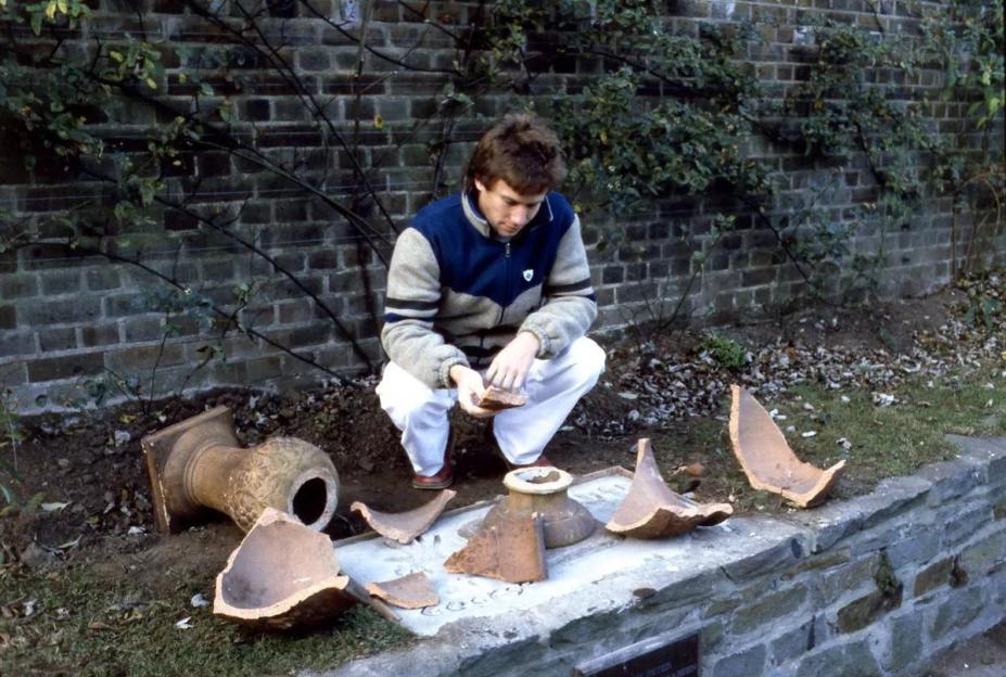 A person examining the broken pieces of a large terracotta pot.