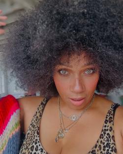 Close-up portrait of a woman with an afro wearing a leopard print top and necklaces.