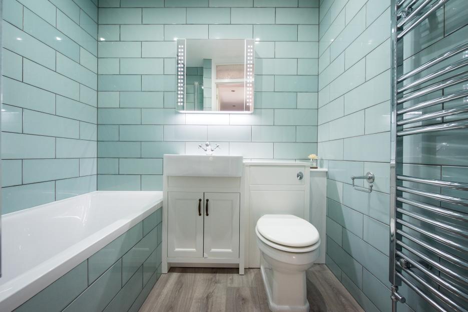 Small bathroom with light teal tile, white fixtures, and chrome towel rack.