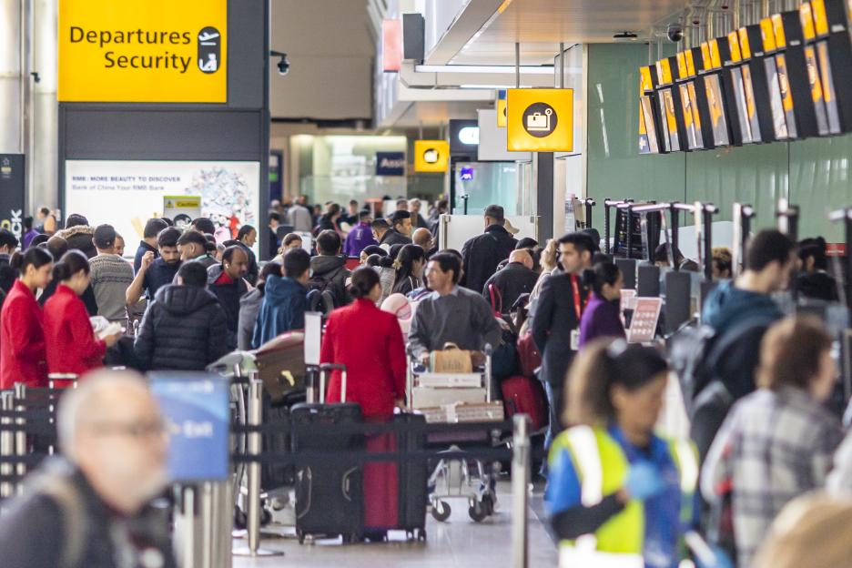 Crowded Heathrow Airport departures security area.