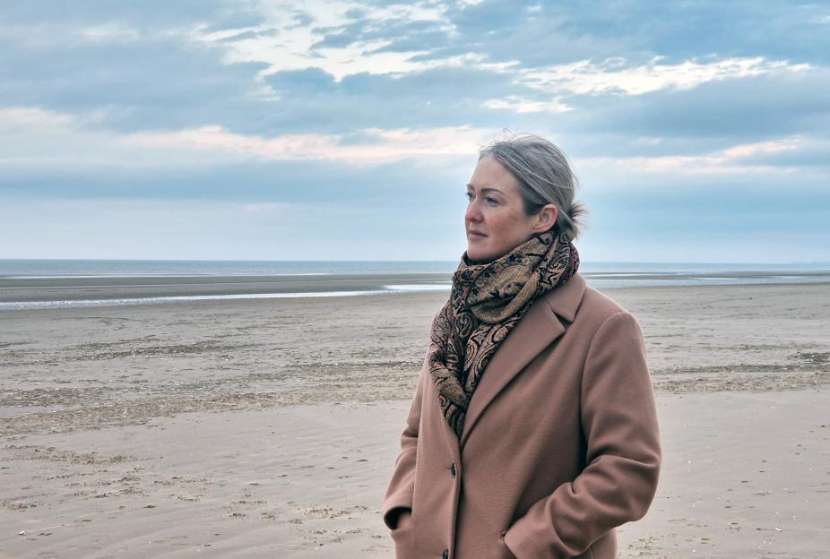 Woman in a coat standing on a beach.