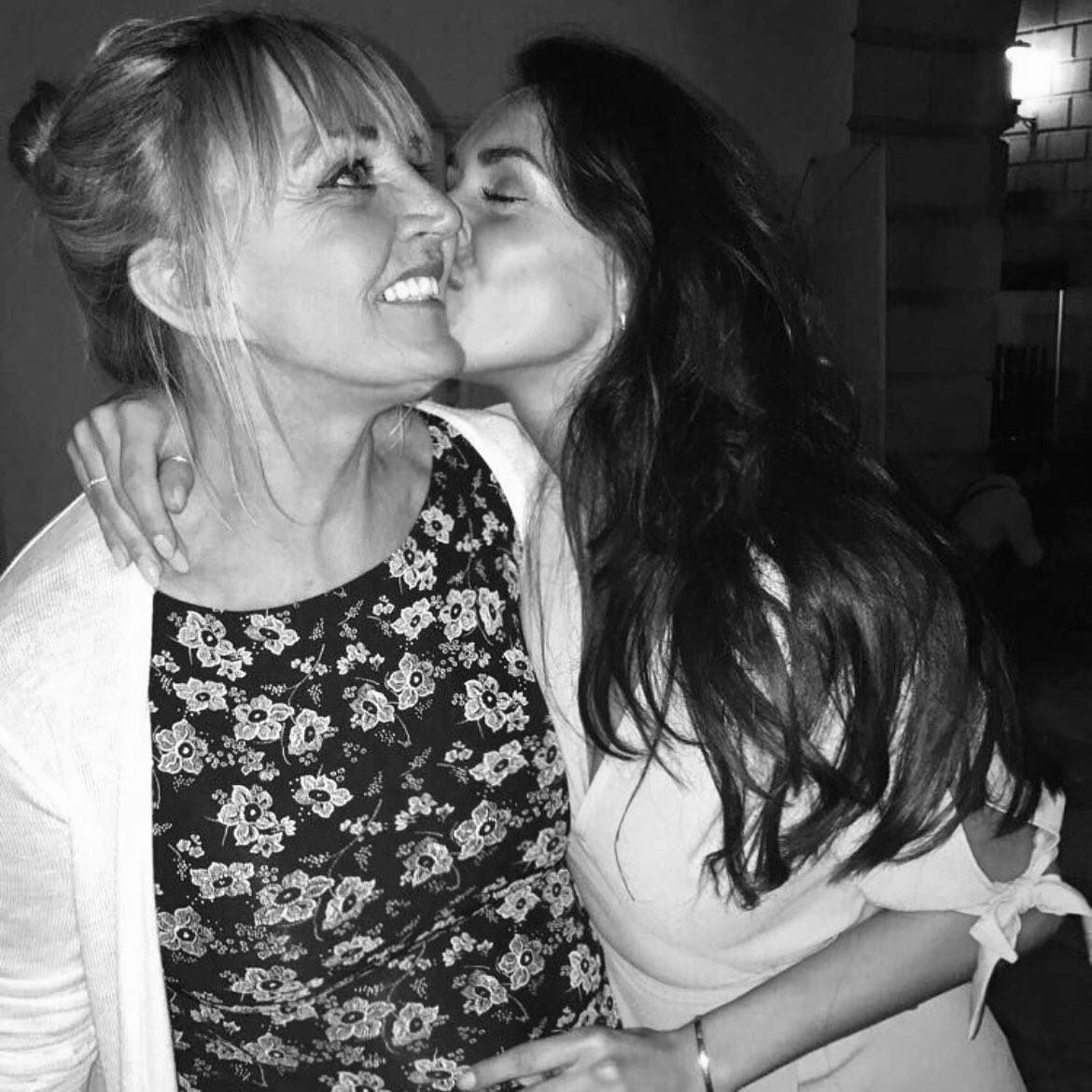 Black and white photo of a young woman kissing her mother on the cheek.