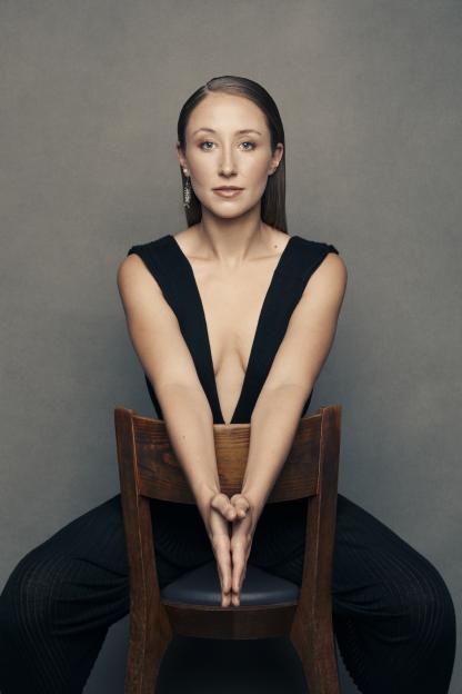 Portrait of Erin Doherty sitting in a wooden chair.