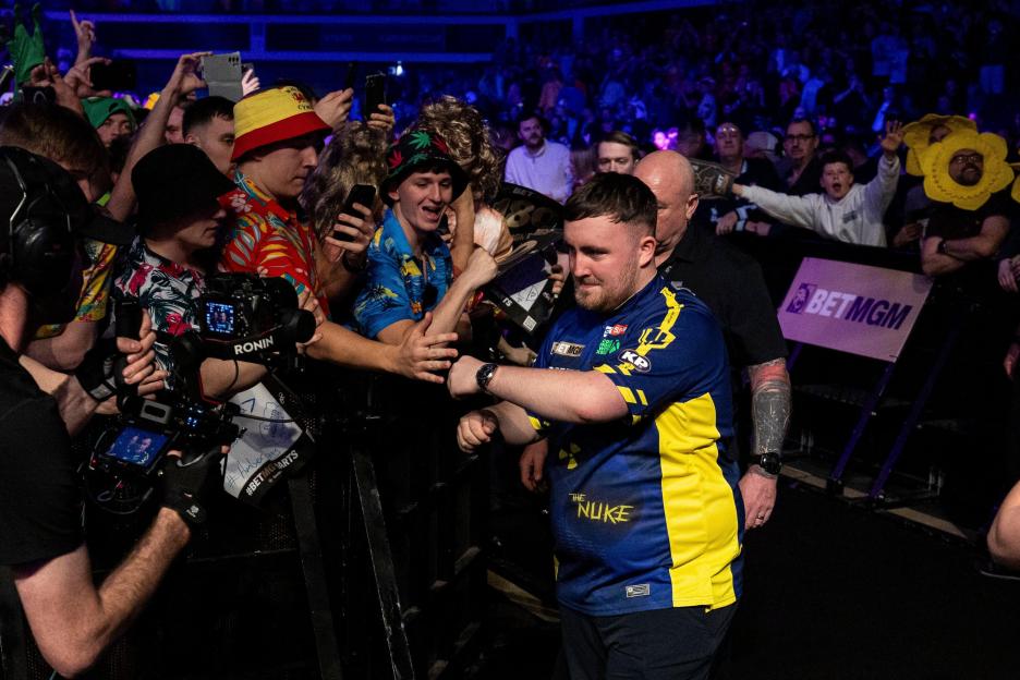 Luke Littler at a darts match, surrounded by fans.