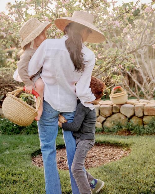 Woman carrying a young child while another child holds onto her leg.