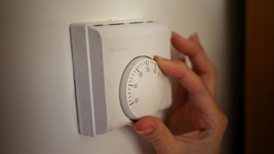 Hand adjusting a central heating thermostat.