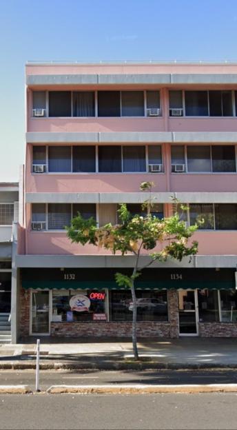 Street view of two buildings, one light grey and one light pink, with businesses on the ground floor.