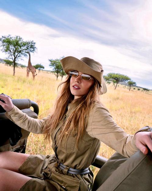 Woman in safari outfit on a game drive, giraffe in background.