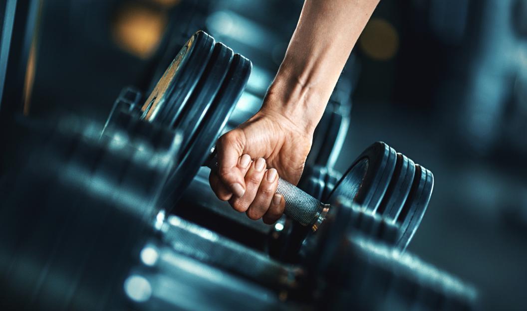 Close-up of a person's hand lifting a dumbbell from a rack.