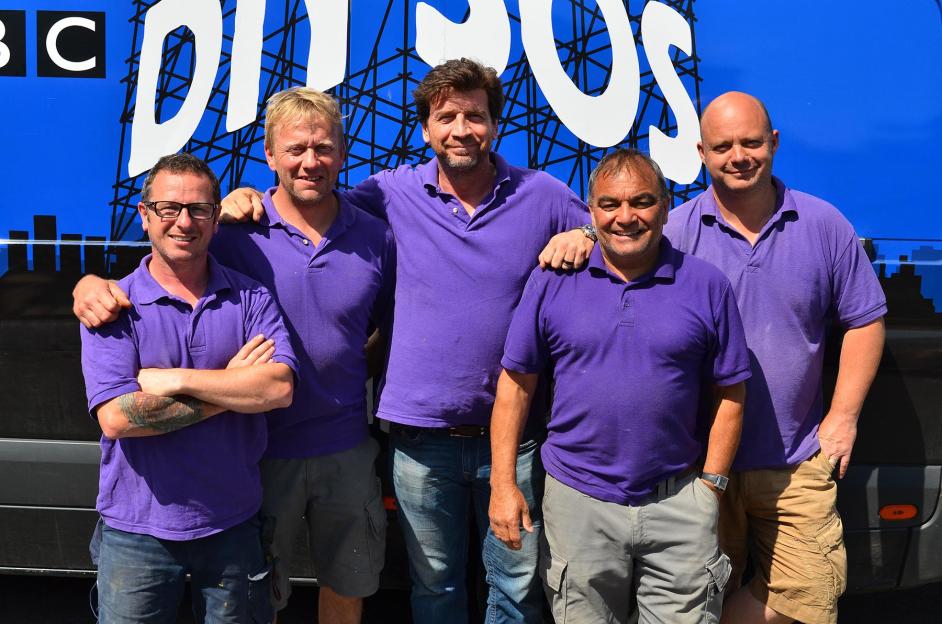 Five men in purple polo shirts stand together in front of a DIY SOS van.