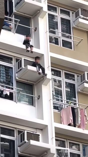 Two boys sitting on a high-rise window ledge.