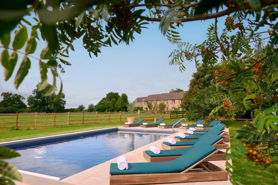 Outdoor pool with lounge chairs and a stone building in the background.