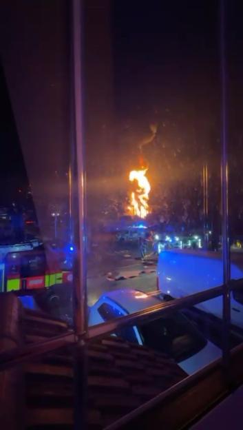 Large fire at night, viewed from a window, with emergency vehicles present.