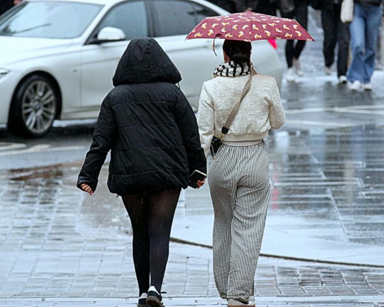 Two women walking in the rain, one using an umbrella.