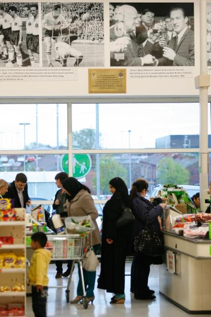 Photo of a memorial plaque in an ASDA store commemorating the 1946 Bolton Wanderers FA Cup match disaster, with shoppers in the foreground.