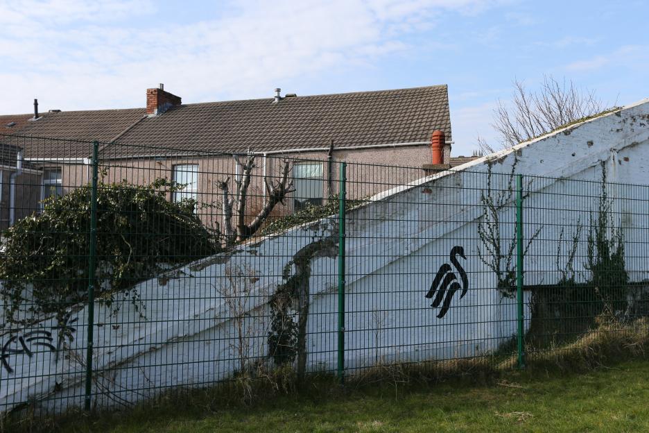 Demolition site of the Vetch Field Stadium, Swansea City's former home, showing a section of the remaining wall with the club's swan logo.