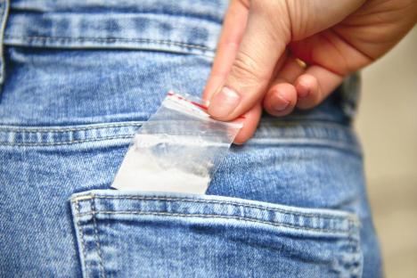 Hand reaching into a jeans pocket to retrieve a bag of cocaine.