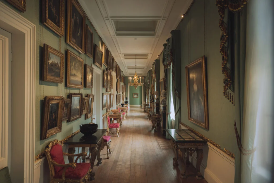 Long hallway with many framed paintings on the walls and antique furniture.