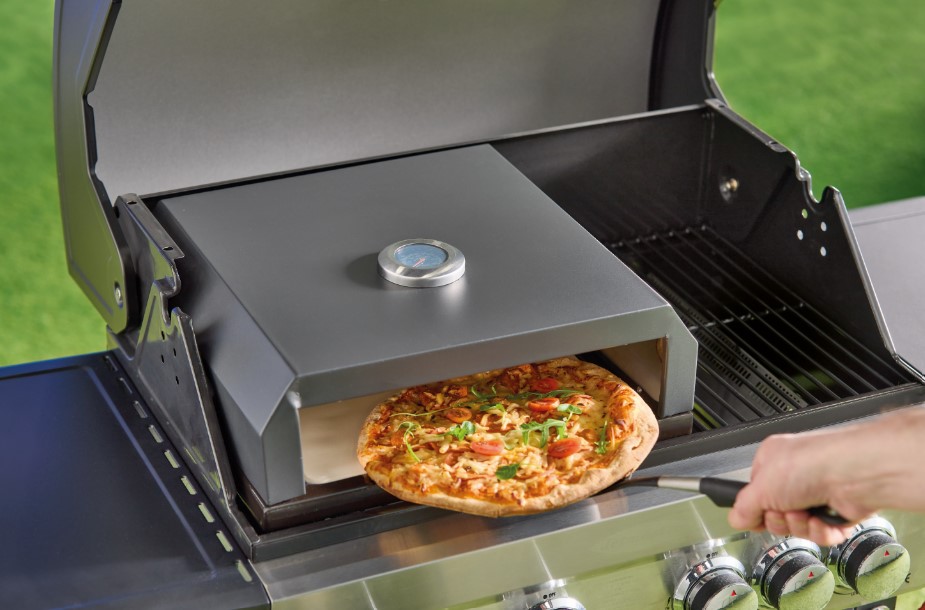 Pizza being removed from a grill's pizza oven.