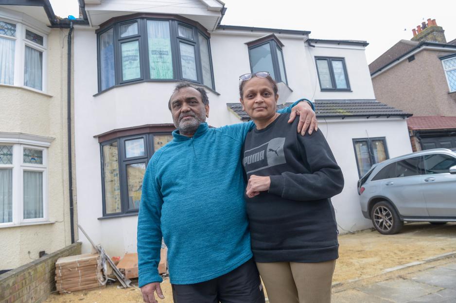 A couple stands in front of their unfinished house.