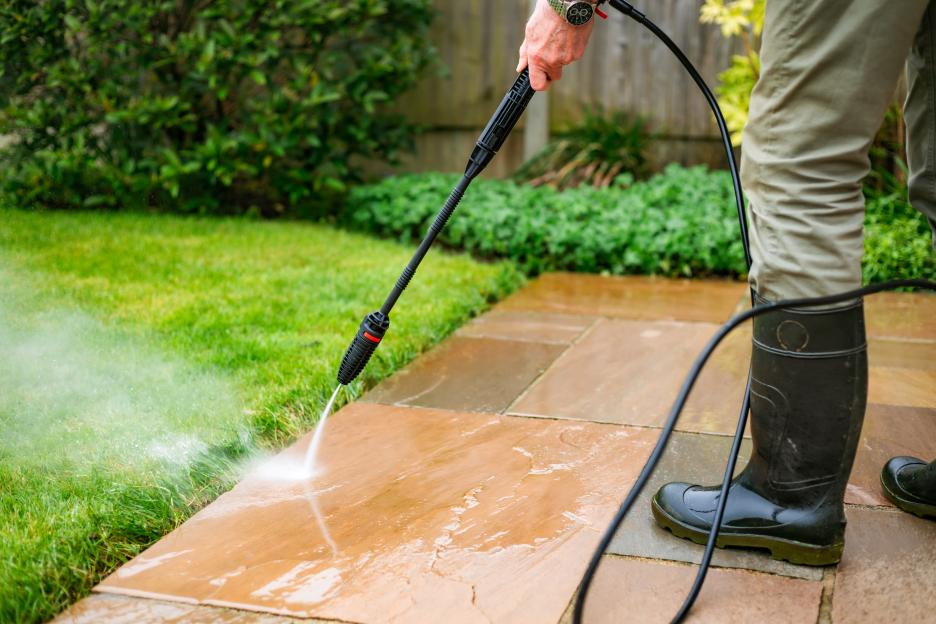 A senior man pressure washing a patio.