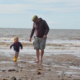A man and toddler walk on a beach.