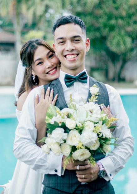 Newly married couple embracing, holding a bouquet.