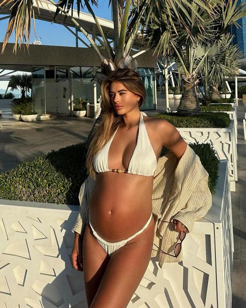 Pregnant woman in white bikini by the beach.