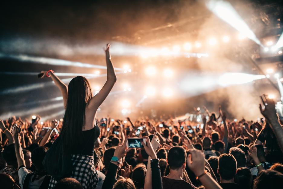 A woman sits on a man's shoulders at a crowded concert.