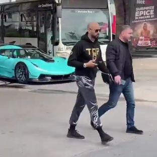 Andrew Tate and another man walking near a teal Koenigsegg.