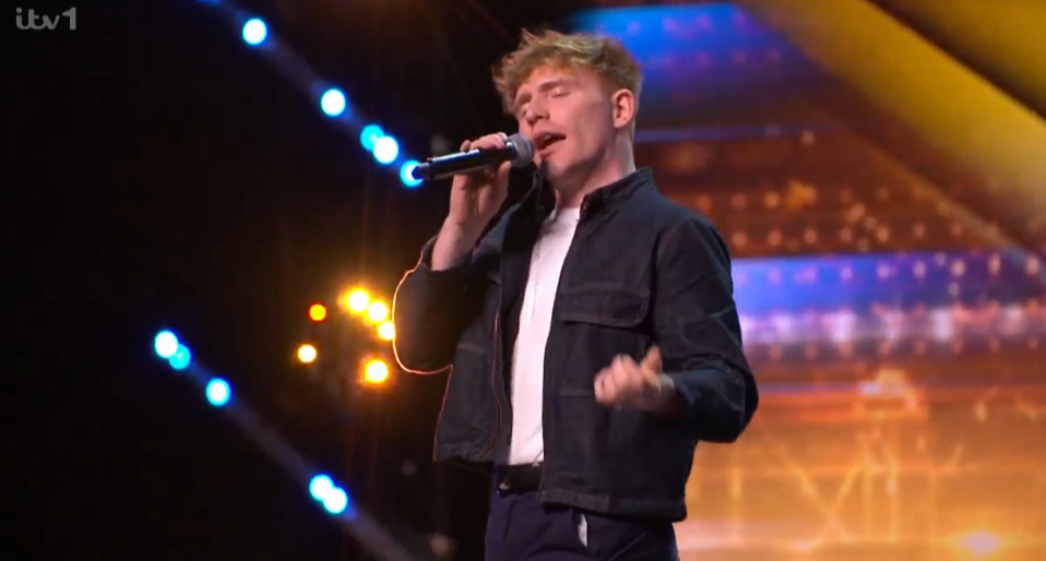 Screenshot of a young man singing into a microphone on a stage.