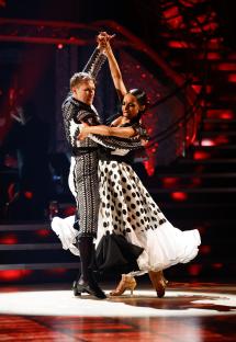 Two dancers in black and white costumes performing a ballroom dance.