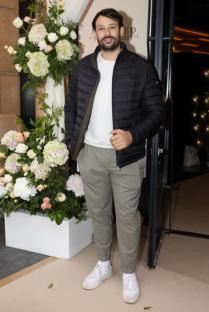 Man in black jacket and light-colored pants standing near flowers.