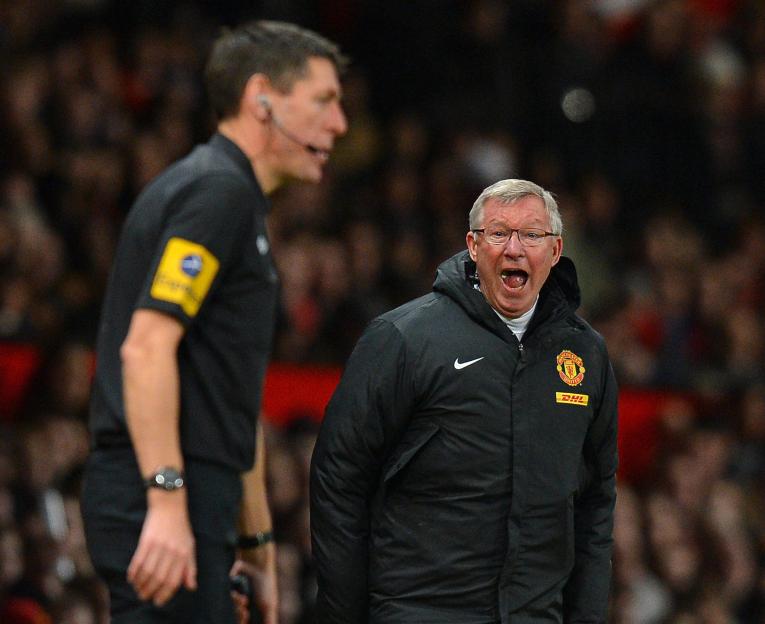 Alex Ferguson shouting at an assistant referee during a soccer match.